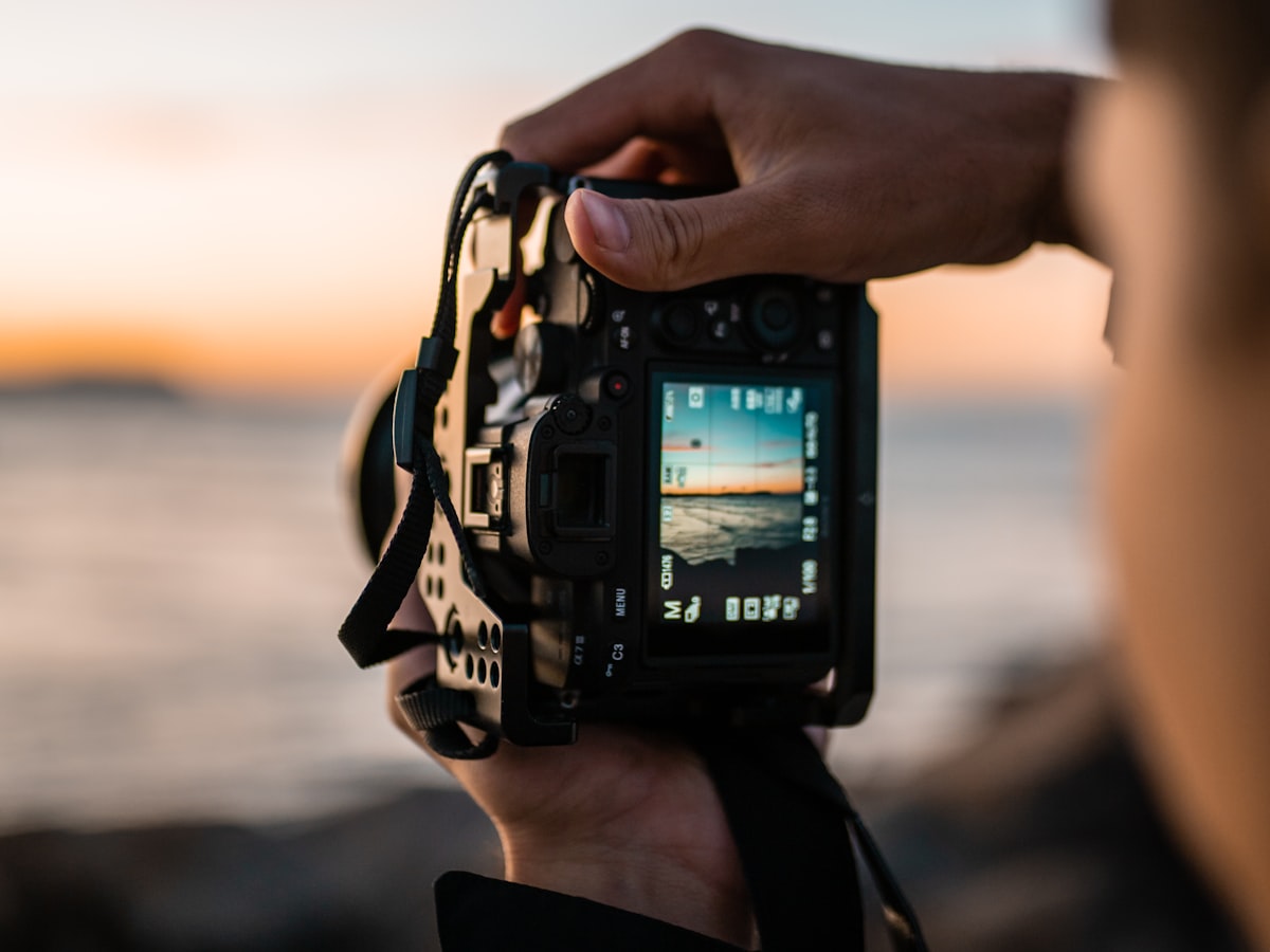 Manos sosteniendo una cámara y encuadrando un atardecer sobre el mar en la pantalla trasera